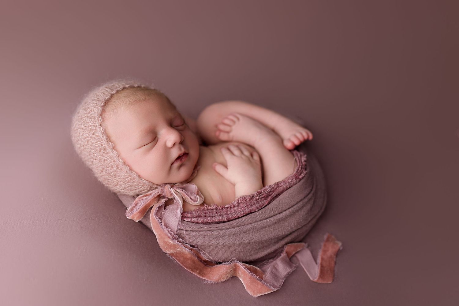 A series of soft, dreamy newborn photography portraits showing a sleeping baby wrapped in pink and mauve fabrics.