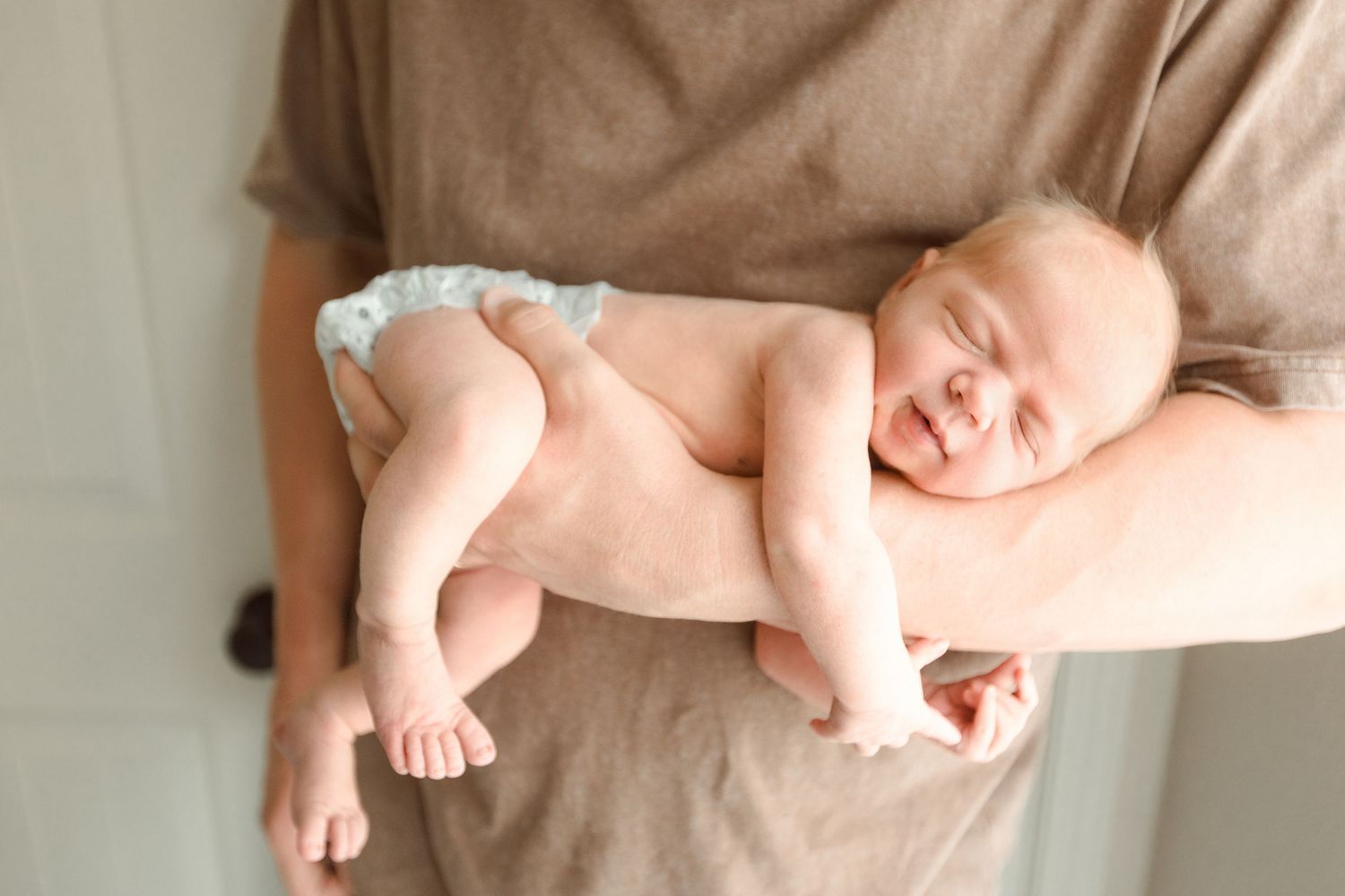 Newborn baby sleeping peacefully on parent's arm in soft natural light during Fresh 48 session in Bridge City nursery.