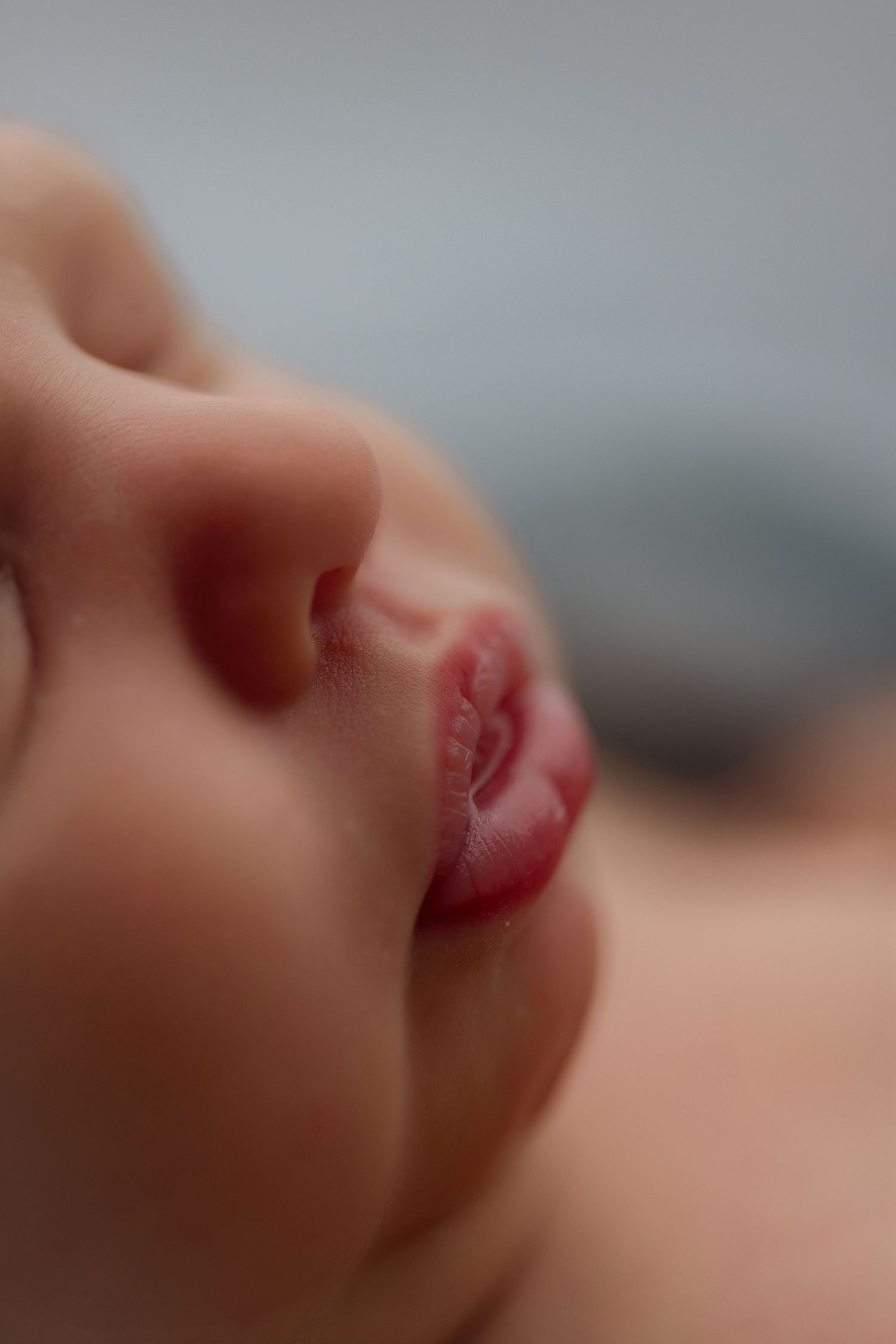 Macro photograph of sleeping newborn's lips and nose with dreamy lighting.