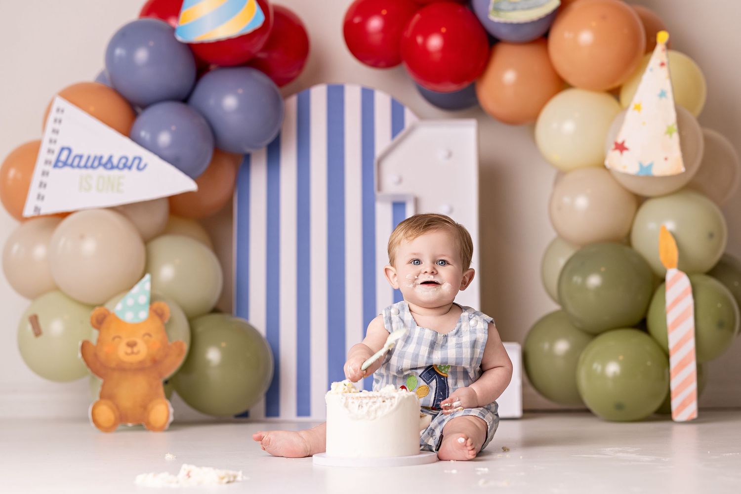 A baby sits on the floor with a birthday cake surrounded by colorful balloons and party decorations.