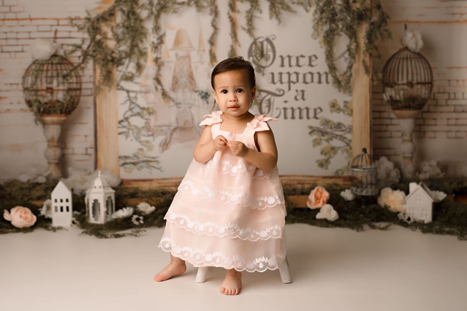 Studio portrait with fairy tale backdrop featuring birdcages and vintage wall text.