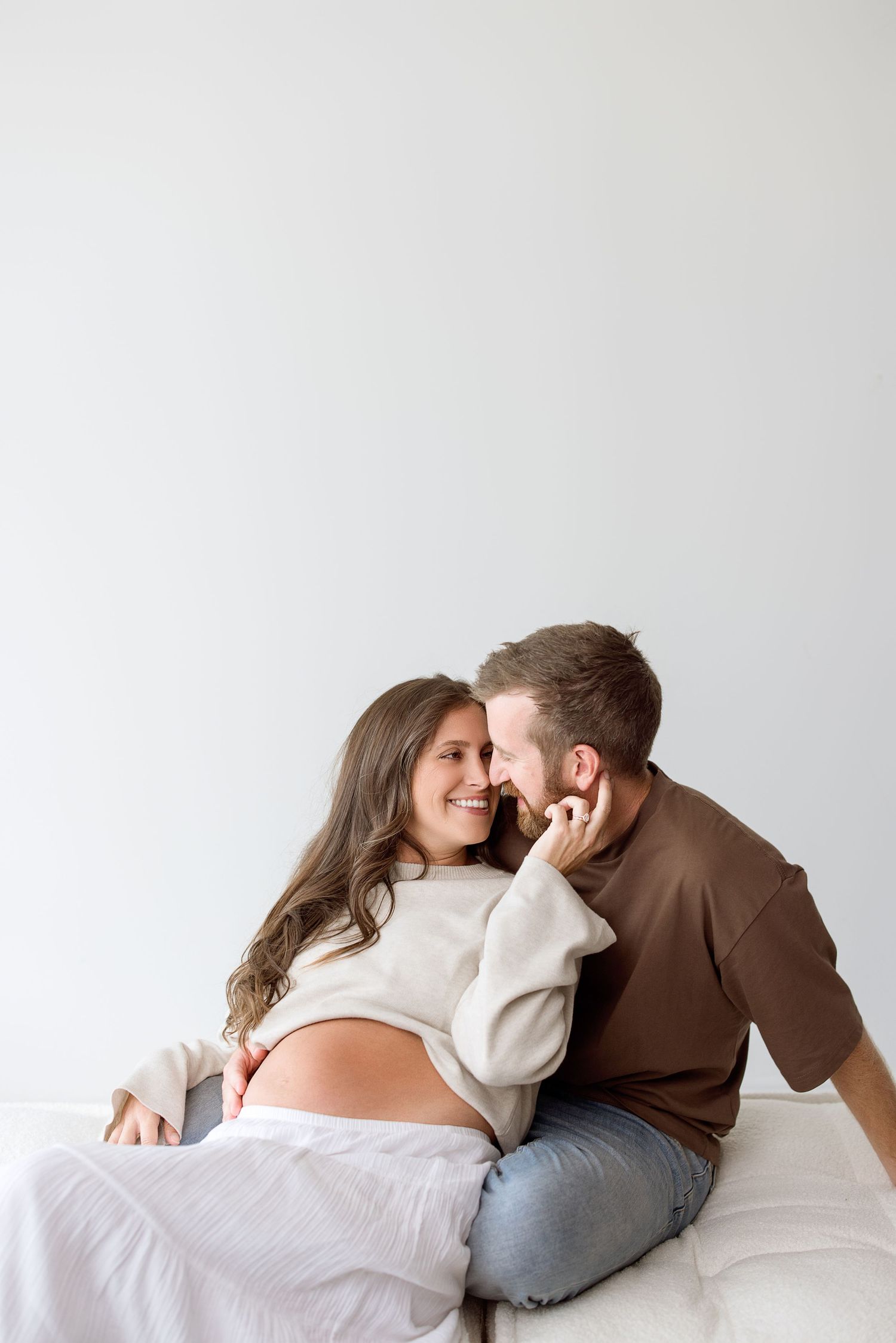 A couple snuggles together on white bedding during an intimate lifestyle photography session.