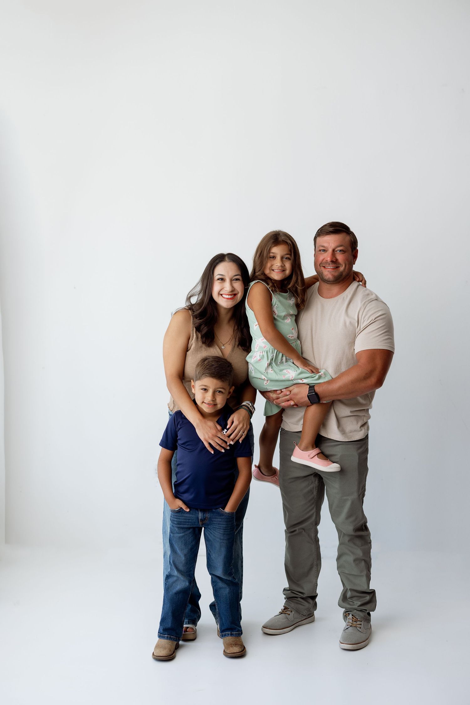 A family poses together against a white background in casual clothing for a studio portrait.