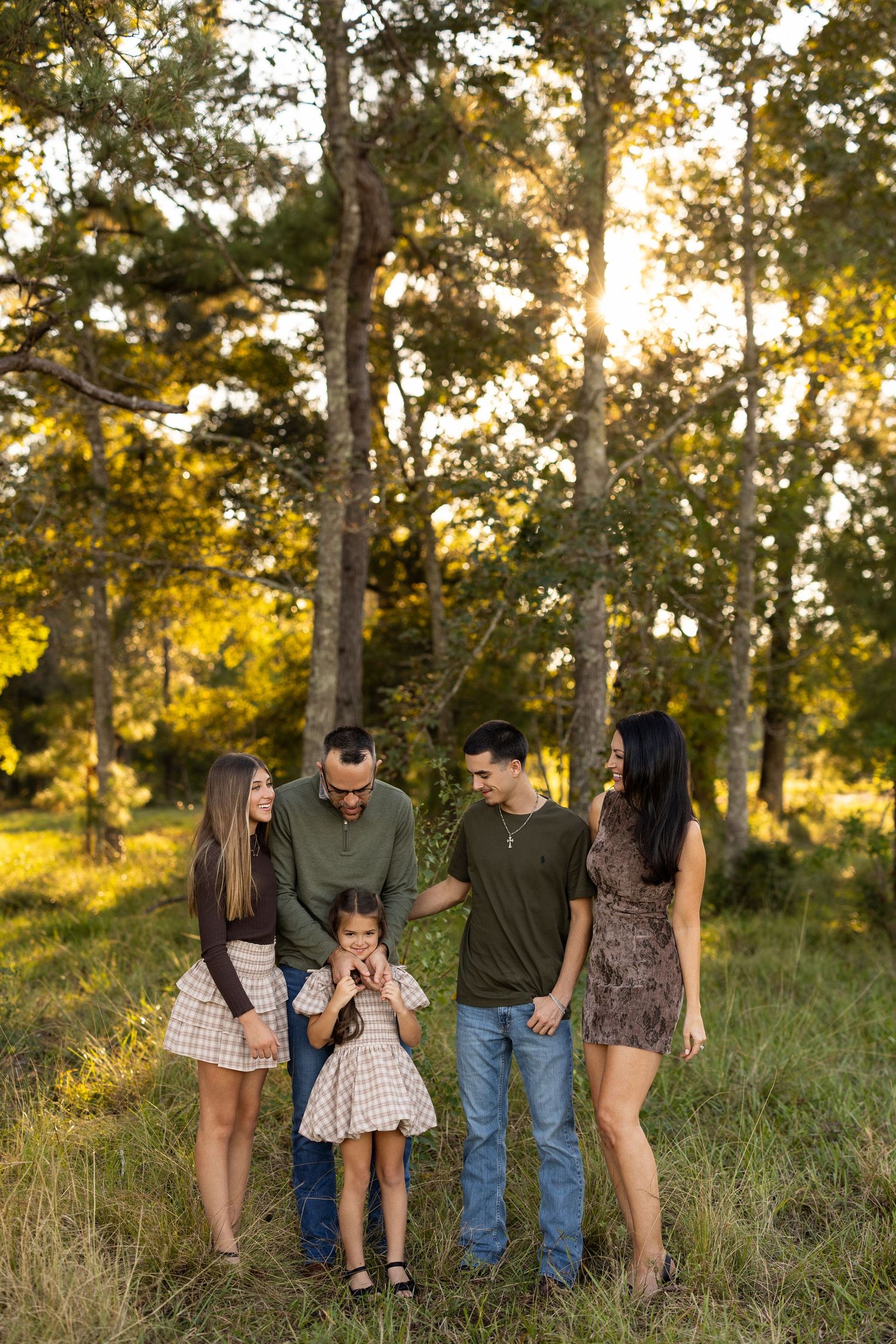 A group walks together through a sunlit meadow with tall grass and trees during golden hour.