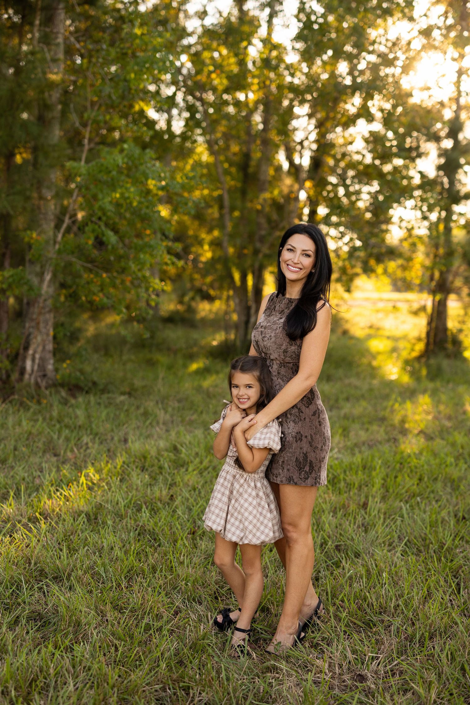 Mother and daughter share playful moments in a sun-drenched forest setting during golden hour.