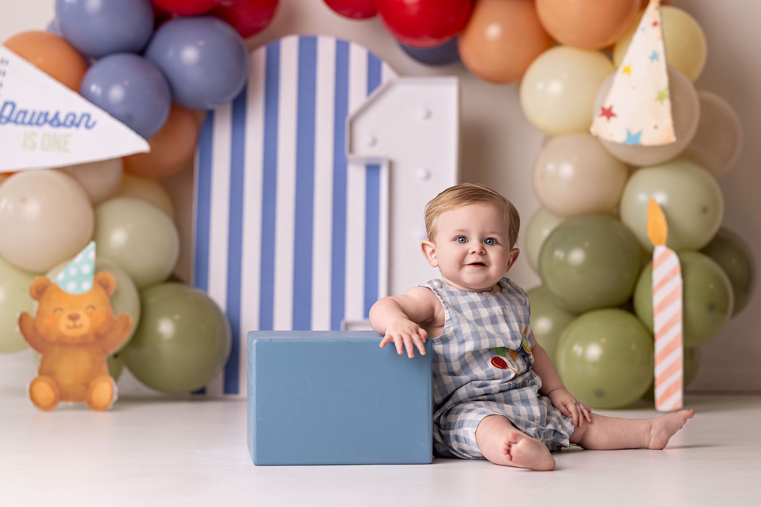 Festive birthday party setup with colorful balloon garland and striped blue and white backdrop for cake smash photos.