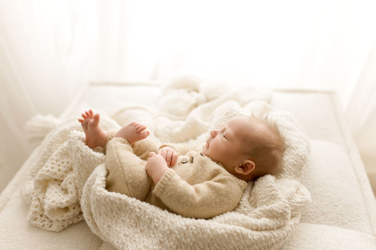 Newborn baby wrapped in soft white blanket sleeping peacefully on light background.