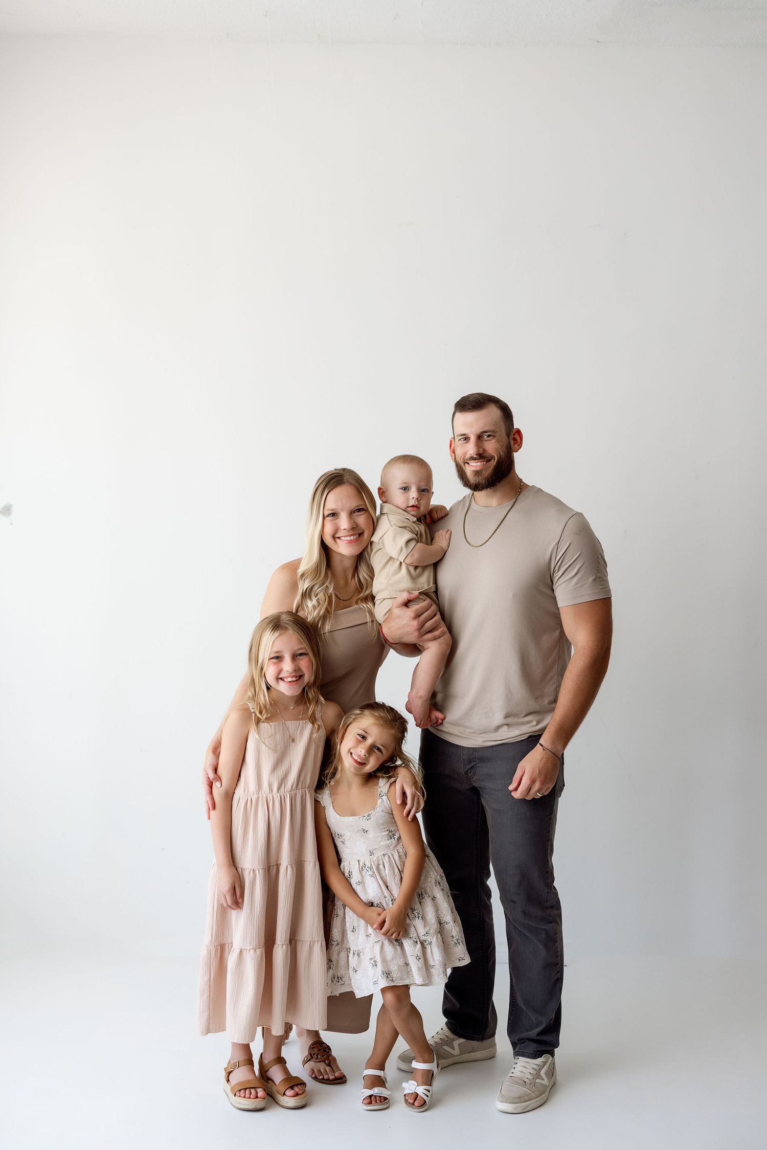 Studio portrait of a family group posing together against a light gray background in casual coordinated outfits.
