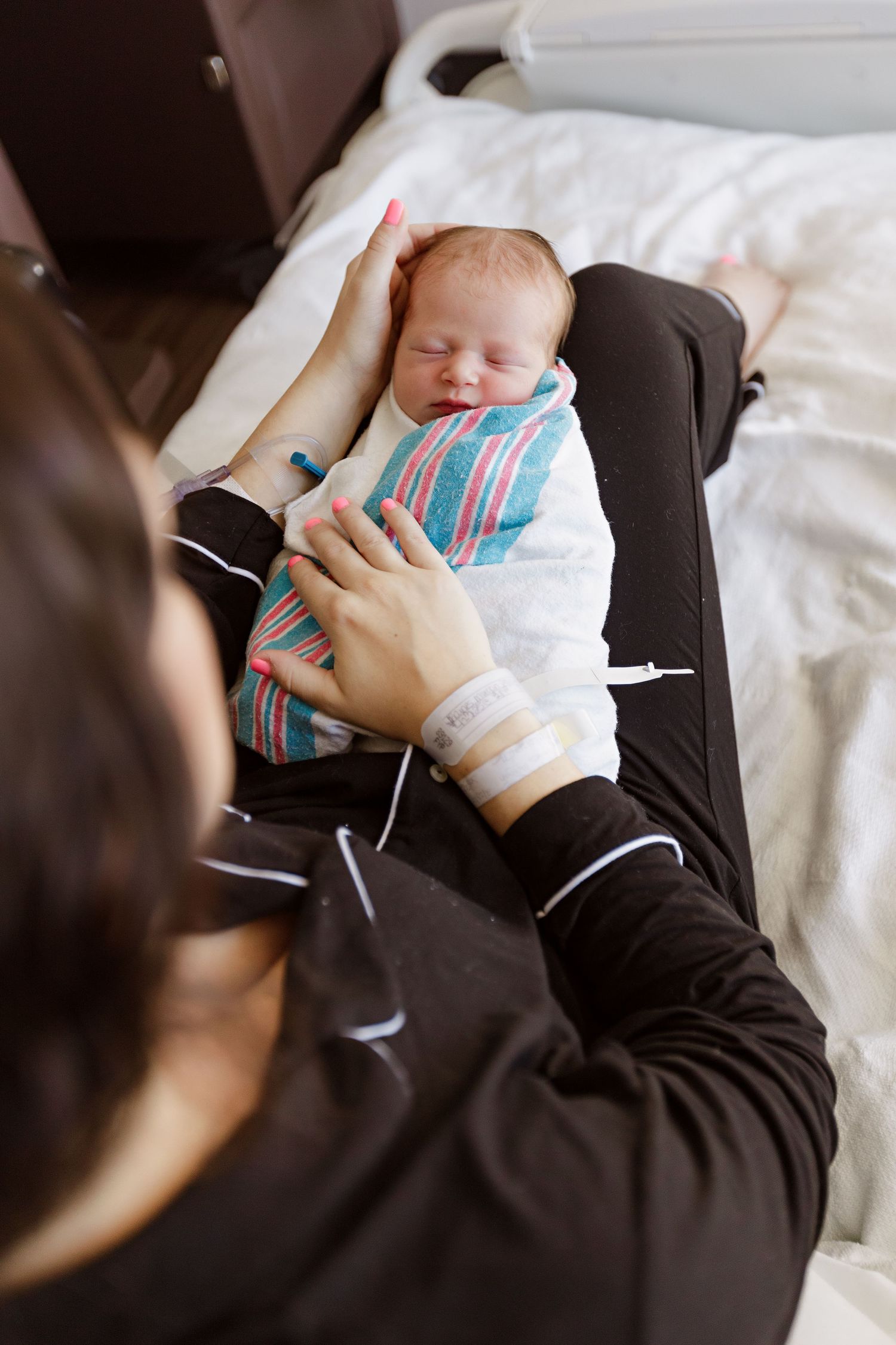 A newborn baby wrapped in a striped blanket rests peacefully while being held in the hospital during Fresh 48 session in Beaumont hospital.
