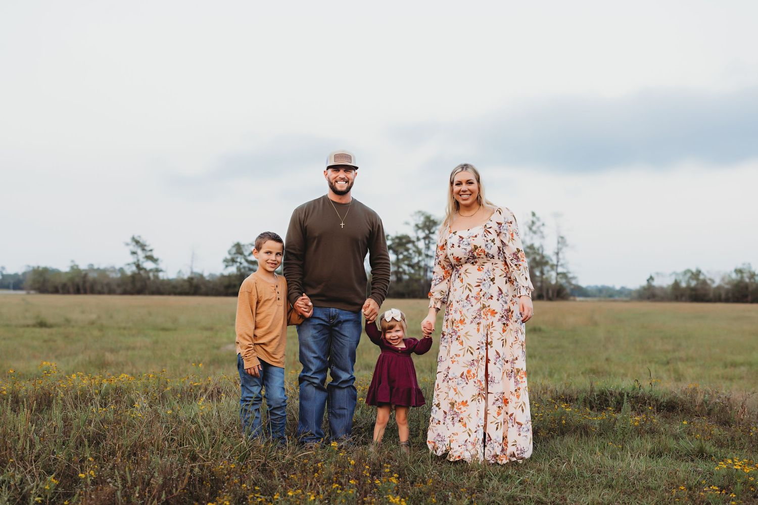 A family of four poses together in a serene meadow landscape at dusk.