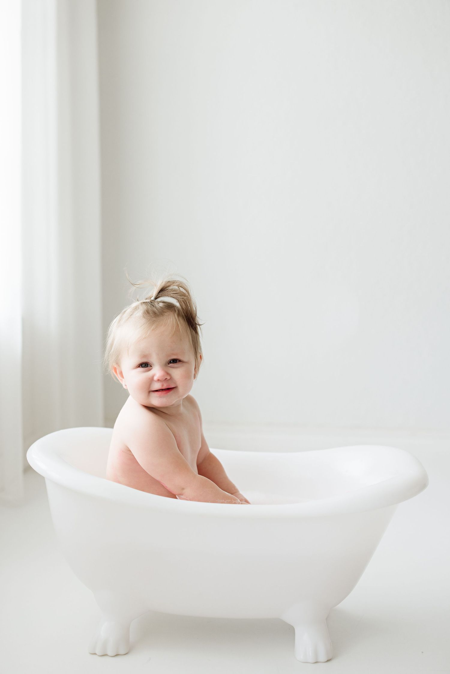 Baby sitting in white vintage-style bathtub during minimalist photo session.
