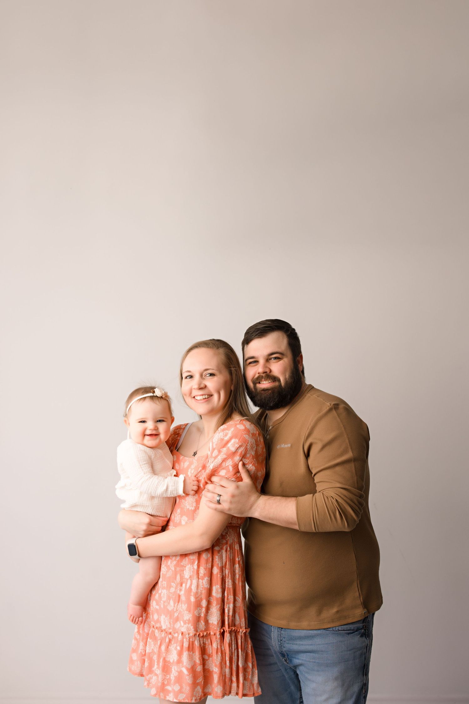 Family portrait session showing warm embrace in neutral tones with peach dress accents against light background.