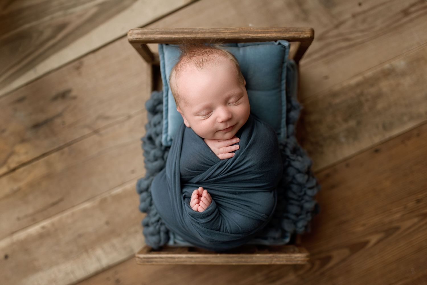 A series of newborn portraits on wooden flooring showing a baby wrapped in blue fabric from different angles.