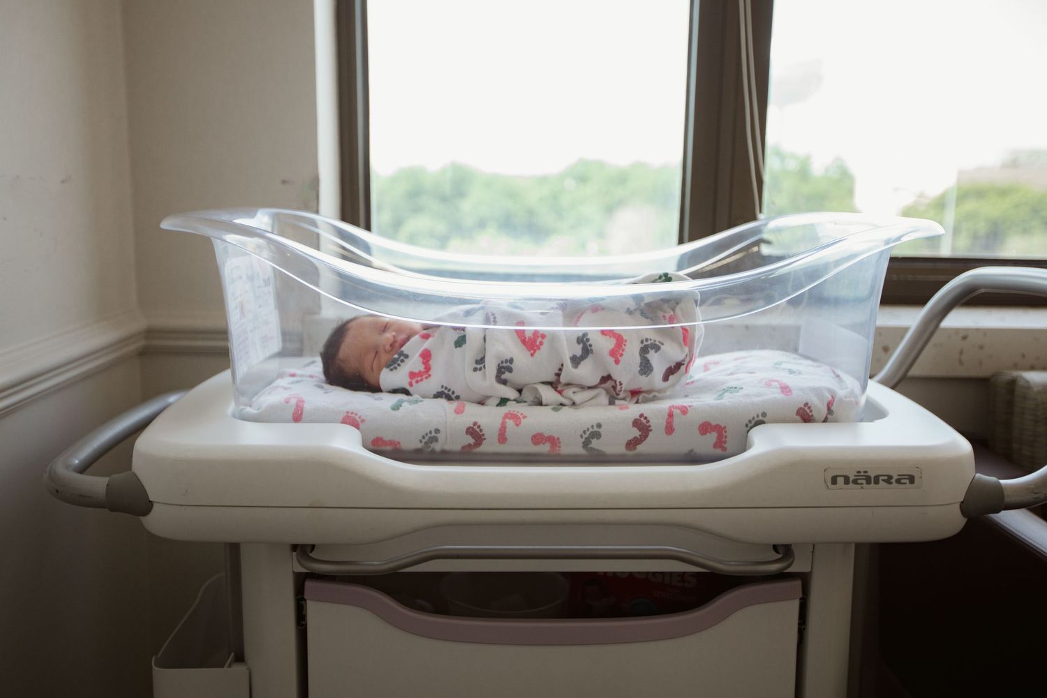 Newborn baby resting on hospital scale wearing white patterned sleepwear.