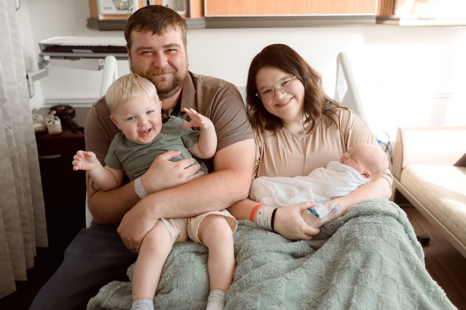 A family shares tender moments while relaxing together on a cozy bed with mint green bedding during Fresh 48 session in Beaumont hospital.
