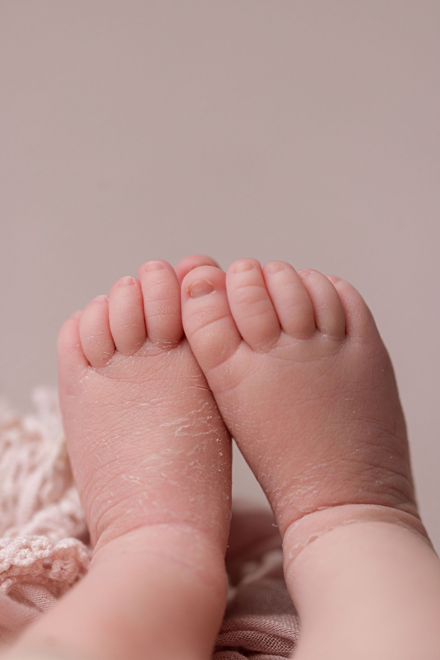 Close-up view of tiny baby feet with delicate toes against a soft pink background.