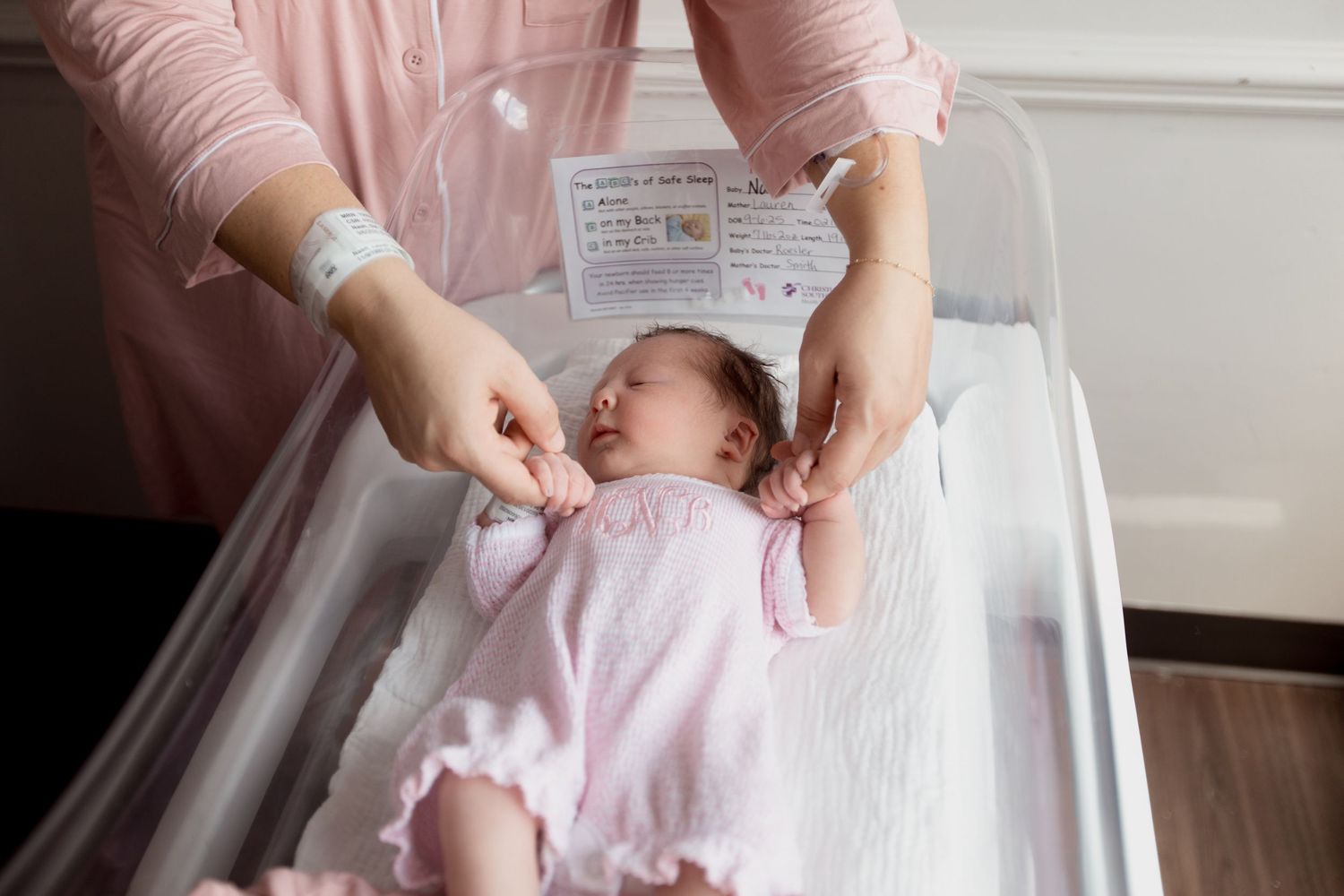 A baby in a pink outfit lies on a changing table while being gently tended to by caring hands.