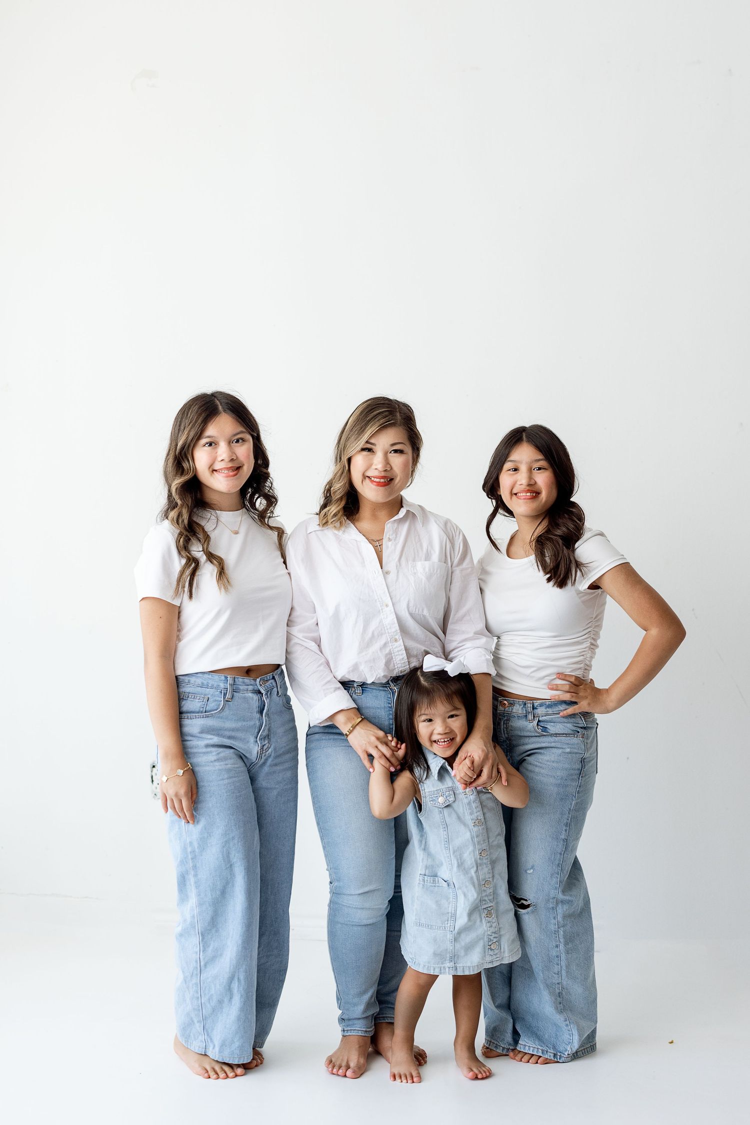 Family group wearing matching white shirts and blue jeans poses playfully against white studio backdrop.