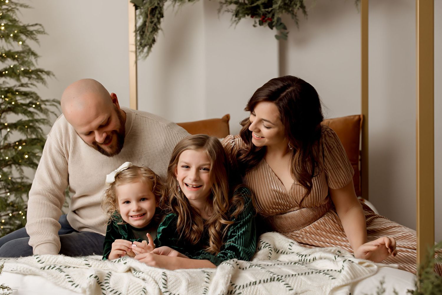 A family shares an intimate moment together on a bed with holiday greenery decorations.