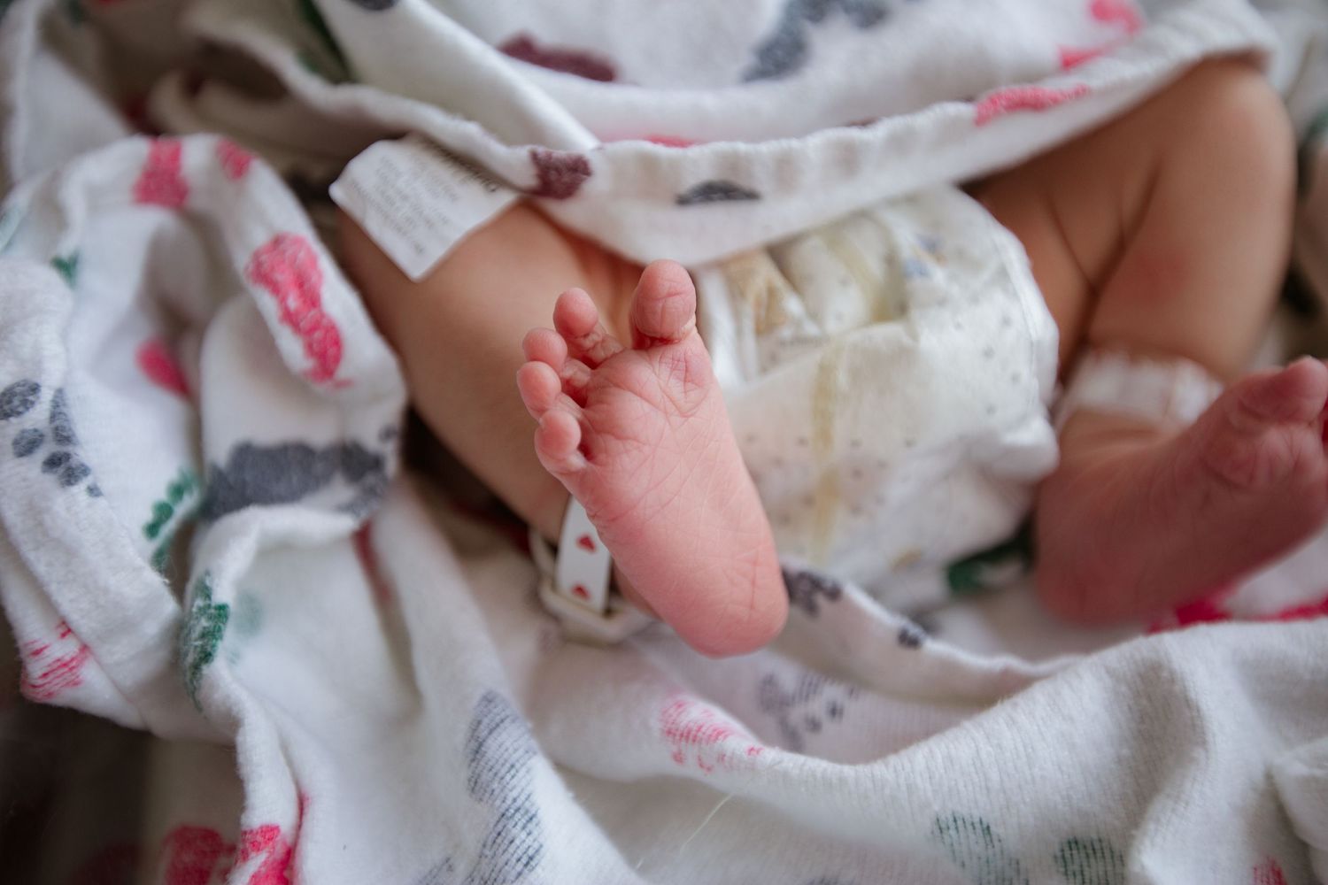 Close-up of tiny newborn baby foot wrapped in white patterned blanket.
