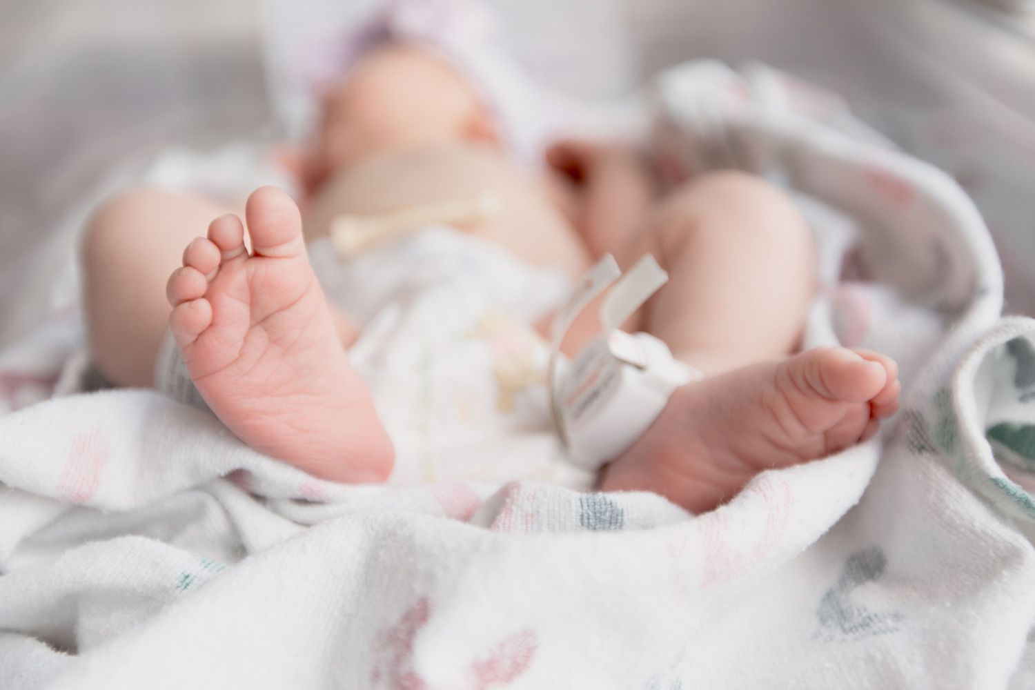 Close-up of tiny baby feet resting on soft white patterned fabric.