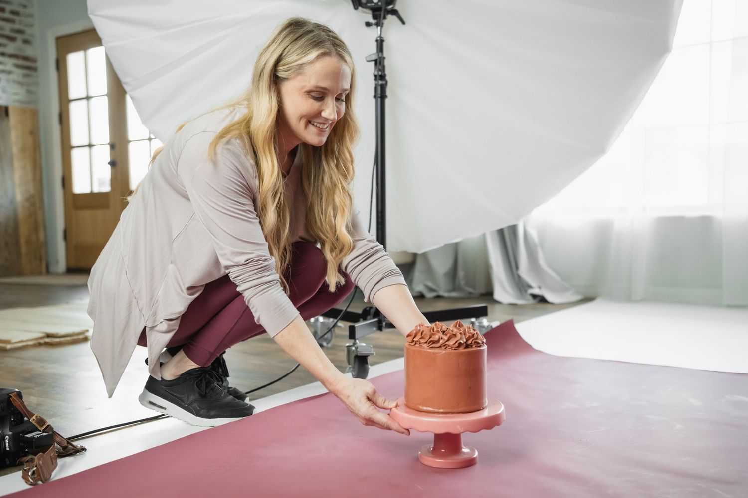Behind the scenes studio setup with photographer preparing pink cake stand.