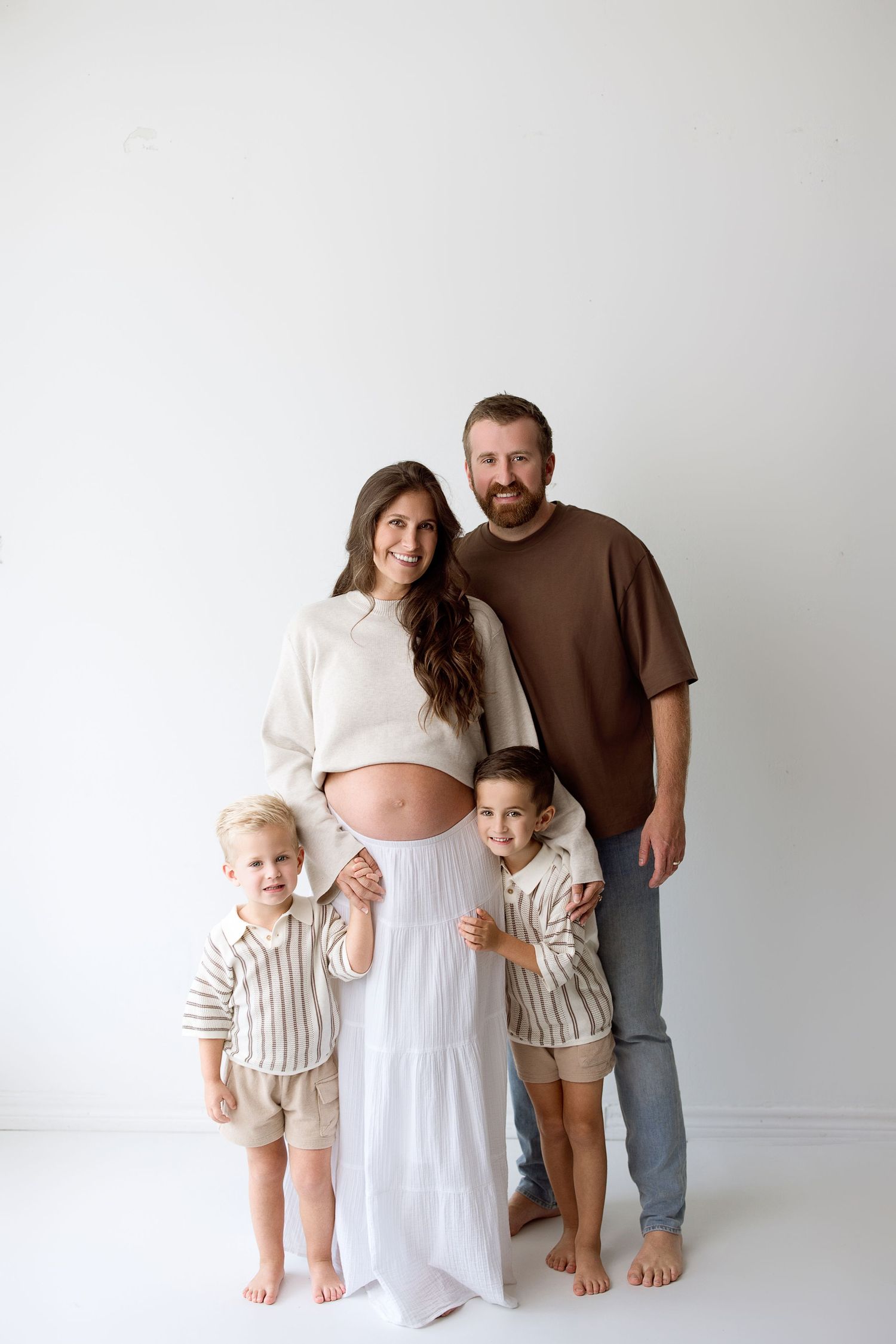 Studio maternity photo sequence showing pregnancy progression with family in neutral tones against white backdrop.