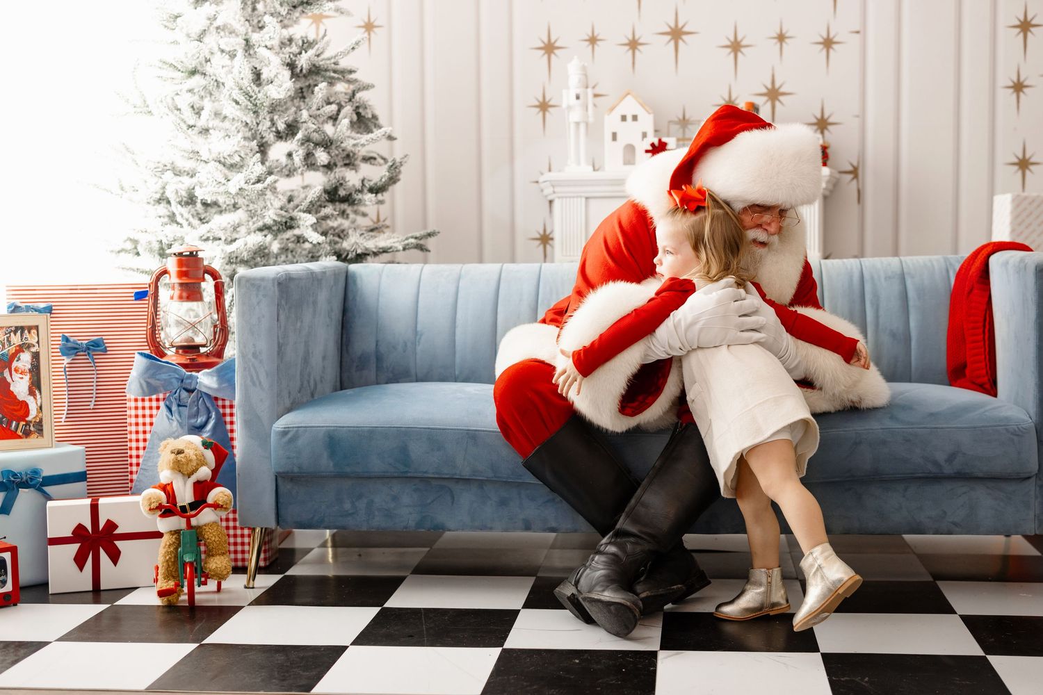 A festive Christmas scene with a decorated tree, blue couch, and someone in a Santa hat arranging holiday decorations.