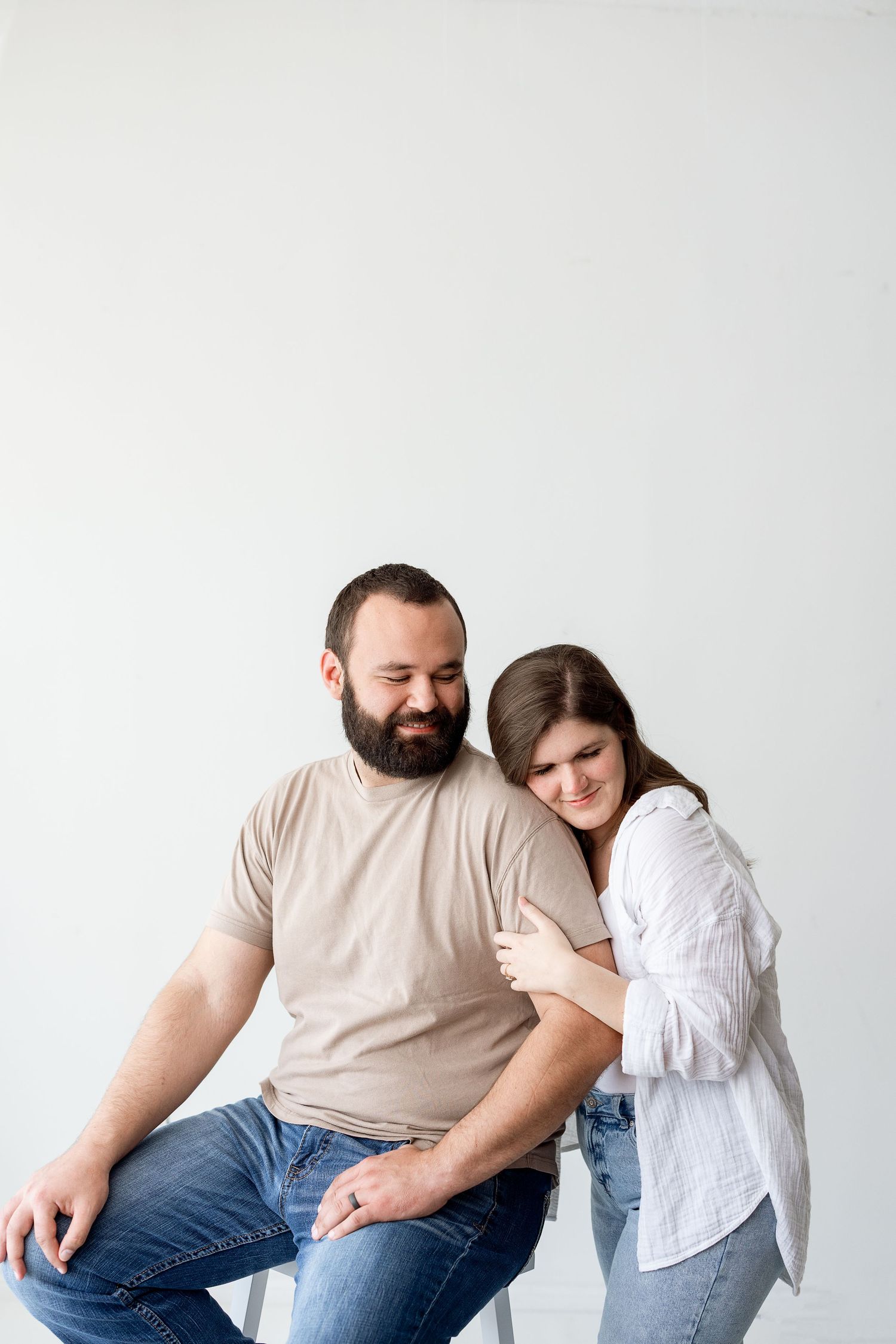A couple in casual attire shares tender moments together in a series of minimalist studio photographs.
