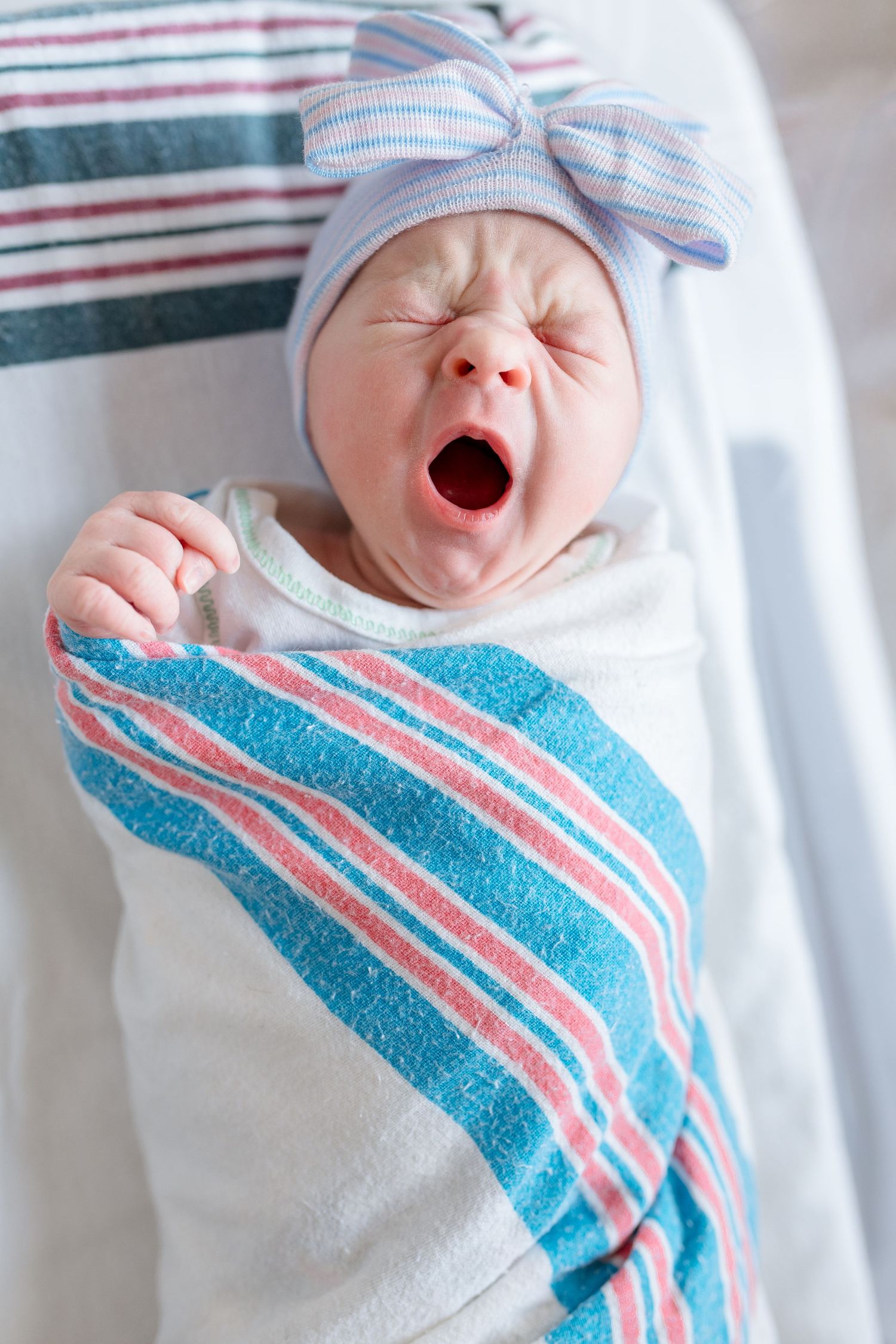 Newborn swaddled in blue and pink striped hospital blanket yawning and sleeping during Fresh 48 session in Beaumont hospital.