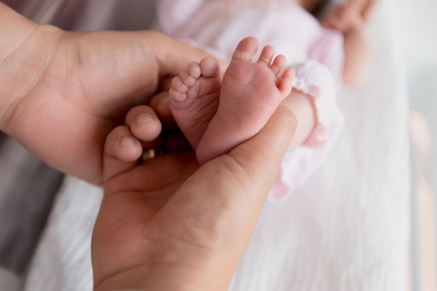 Close-up of a parent gently holding a baby's tiny foot against their hand, showing tender parental care during Fresh 48 session in Beaumont.