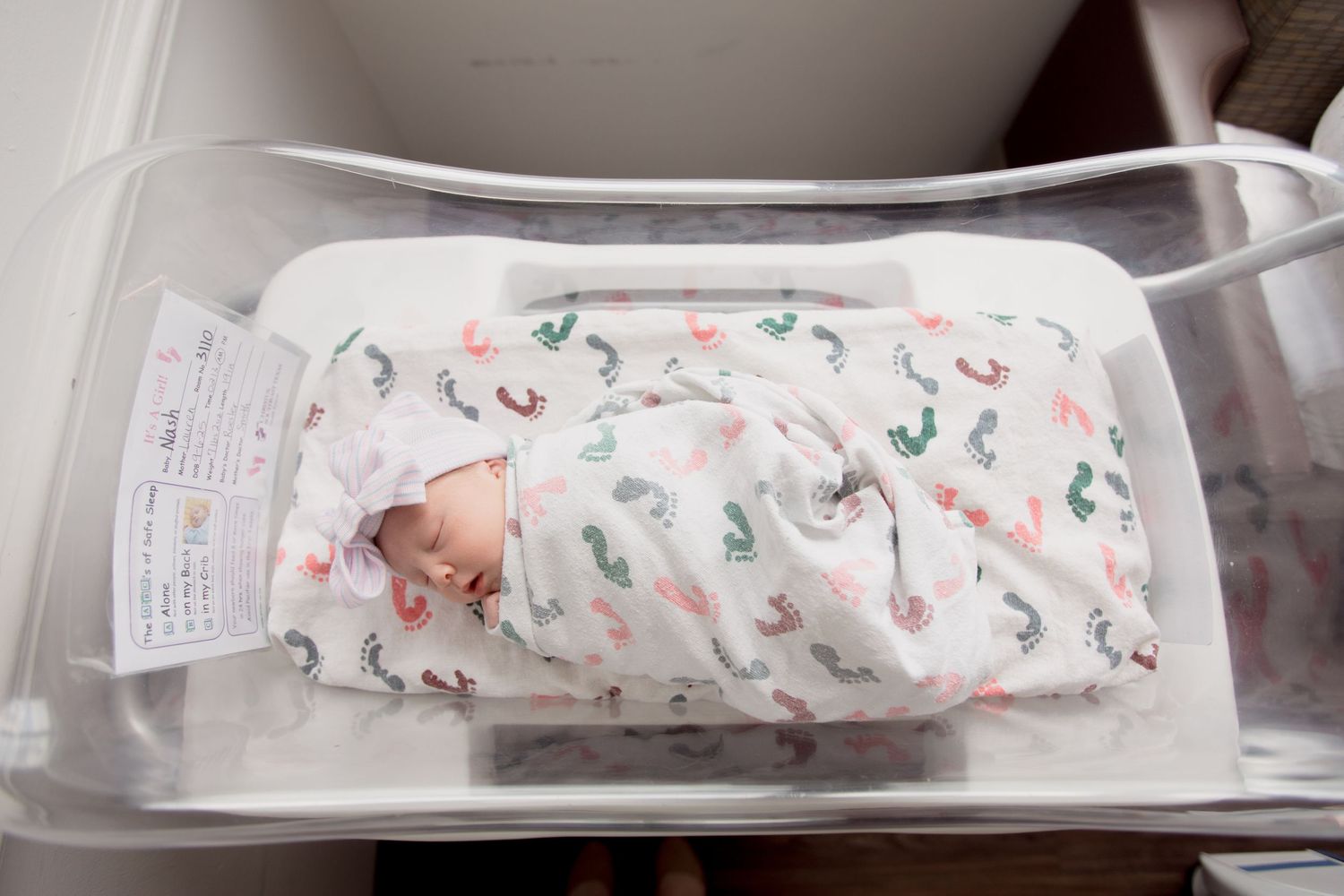 Hospital nursery bassinet with white and pink patterned swaddle blanket and medical equipment.