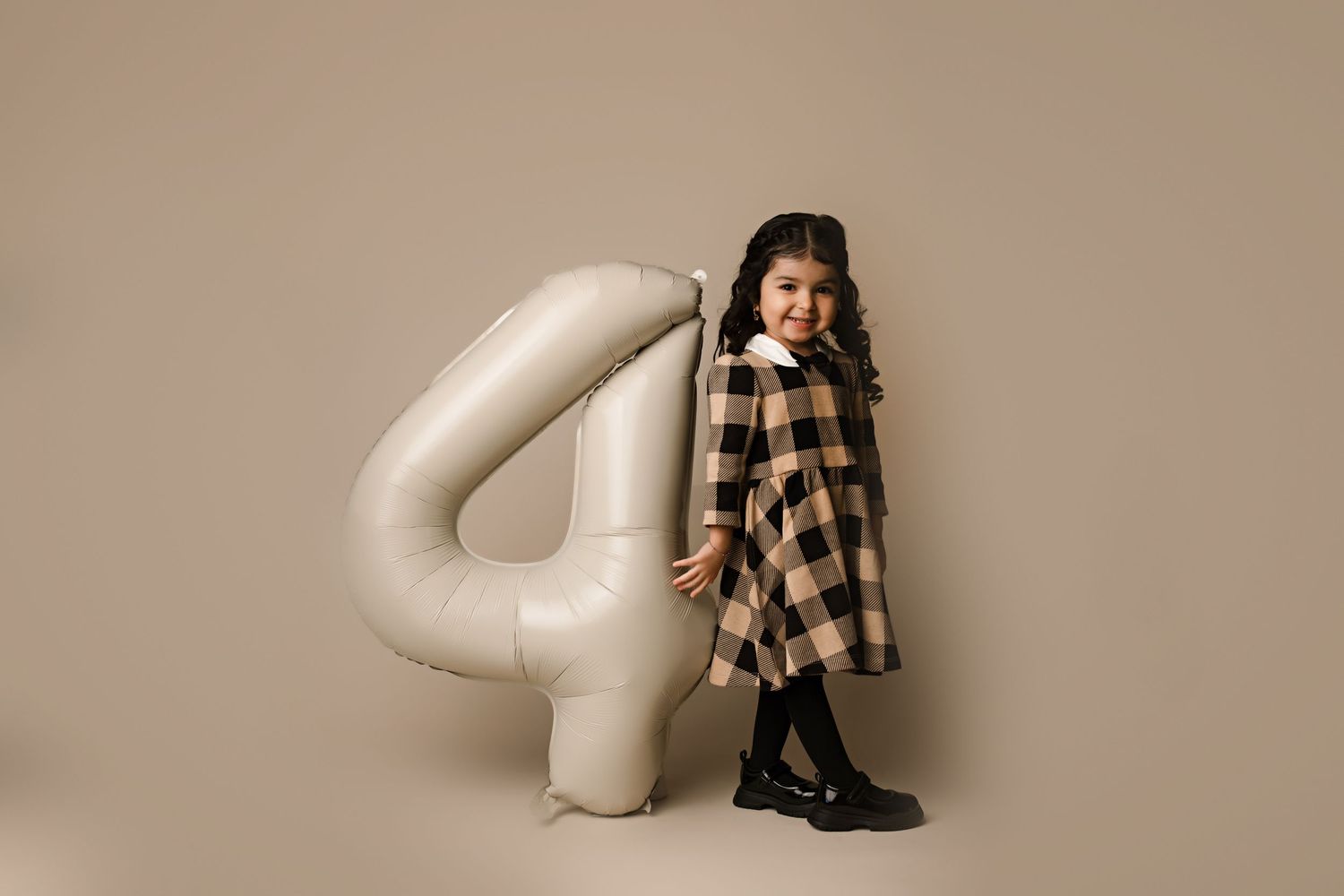Stylized children's photo setup with giant number 4 prop and plaid shirt against neutral background.