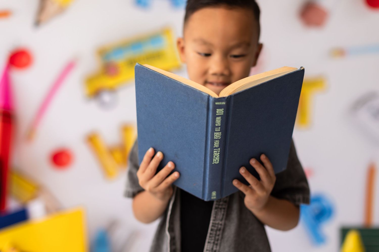 Student reading blue book against colorful educational backdrop with school supplies.