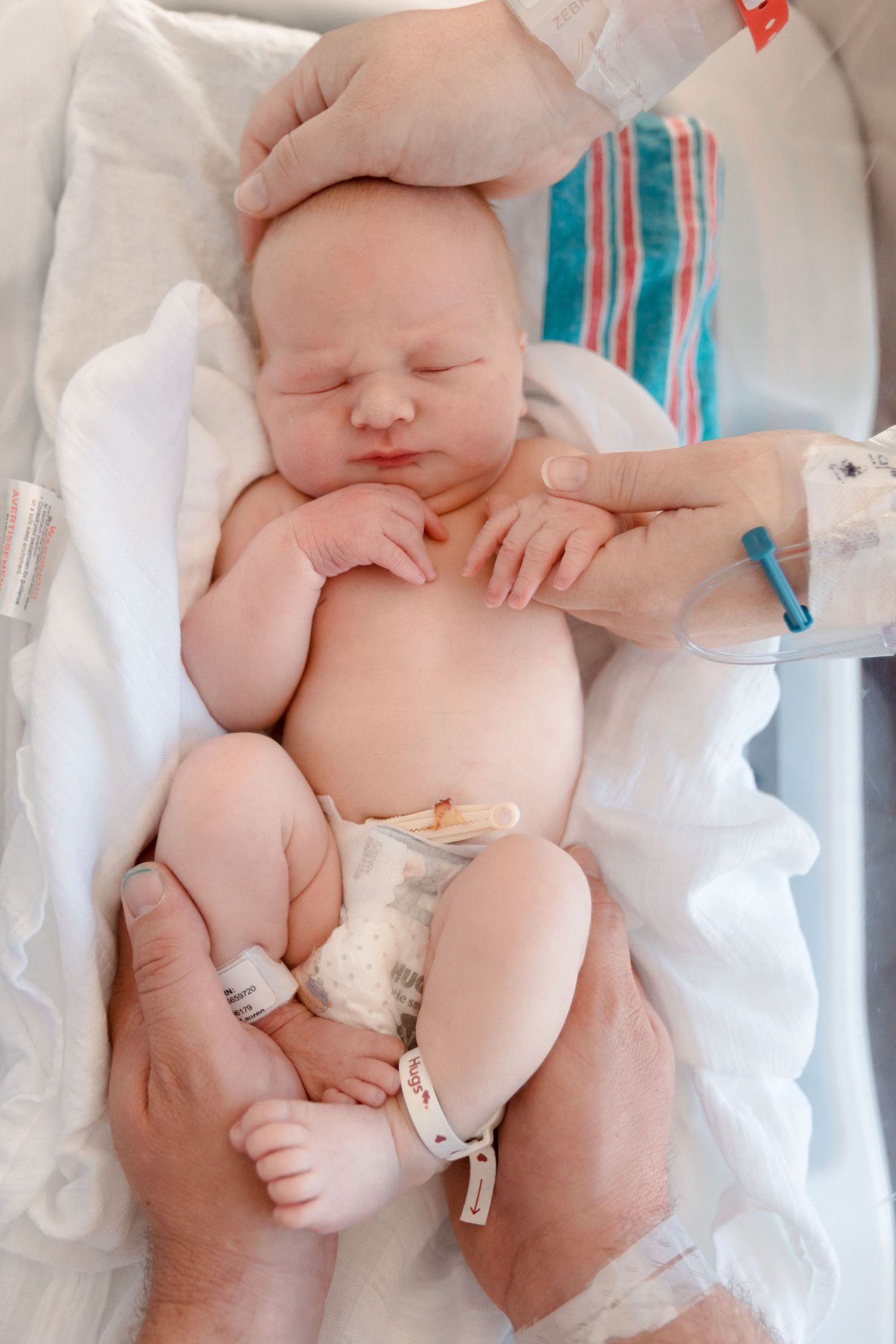 Peaceful sleeping newborn baby wrapped in white blanket with blue and red striped hospital tag visible during Fresh 48 session in Beaumont.