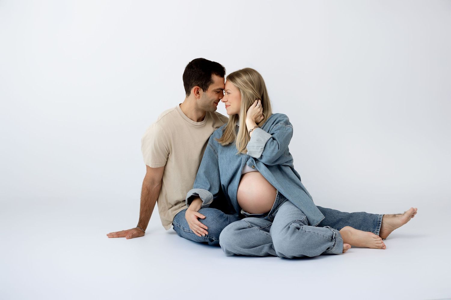 Intimate maternity photo series showing couple in casual clothing embracing on white background with Bree Elle Photography in Nederland, TX.