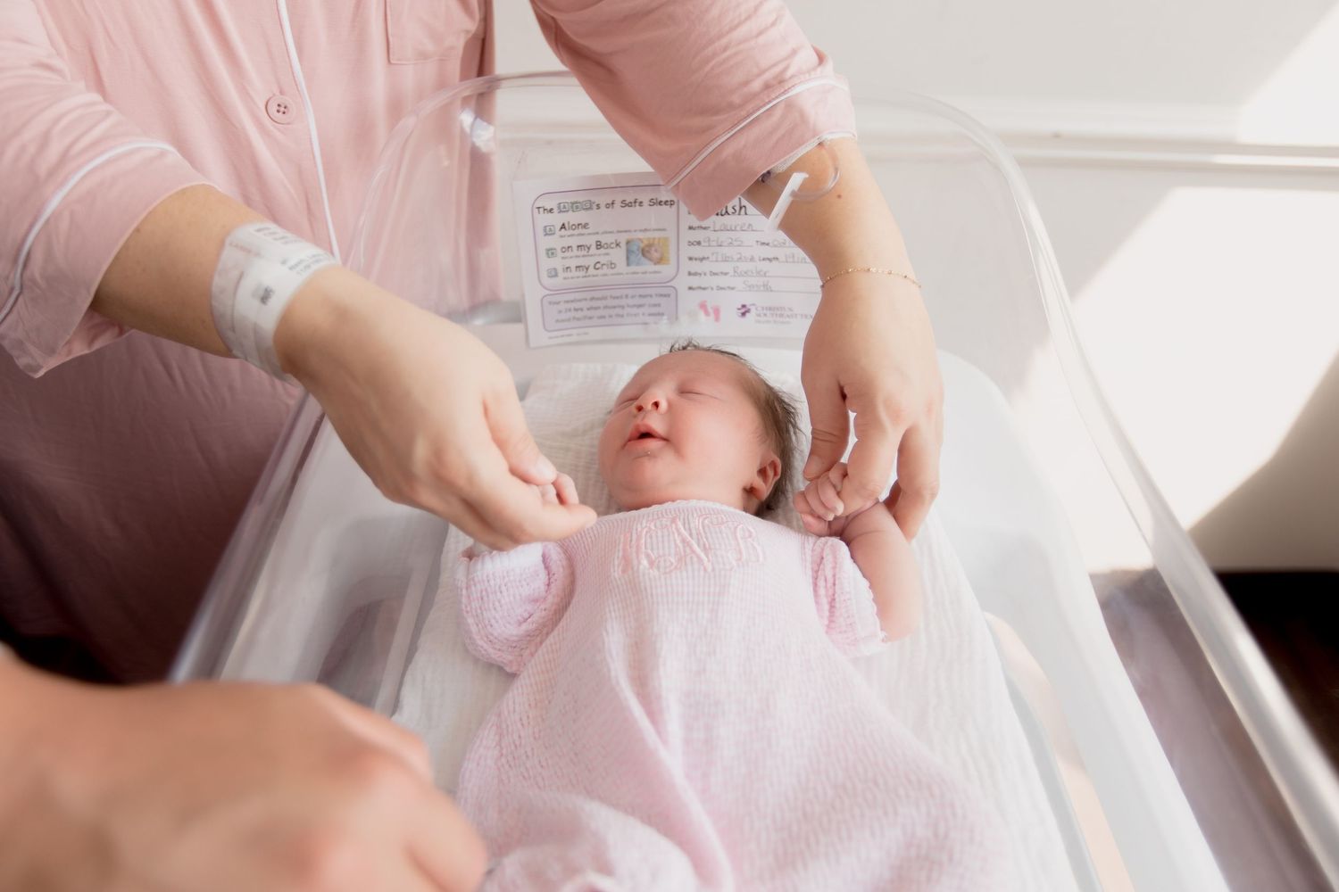 A tender moment in a bright hospital room as a newborn is cradled in soft pink surroundings.