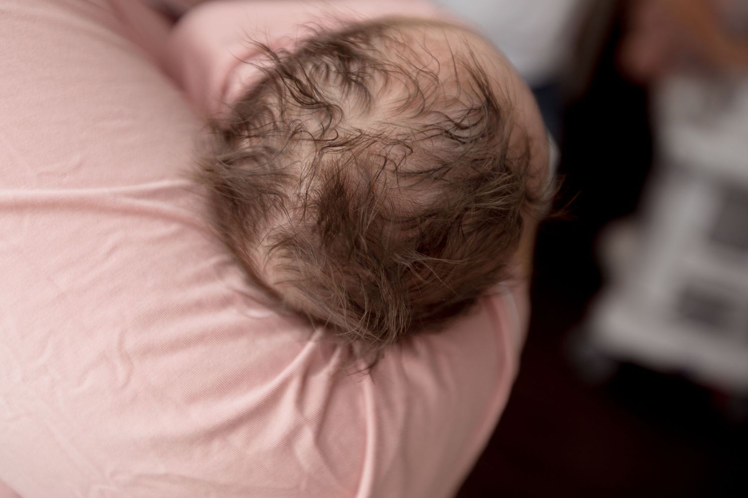 Close-up of a newborn baby's head with fine brown hair against a pink background.