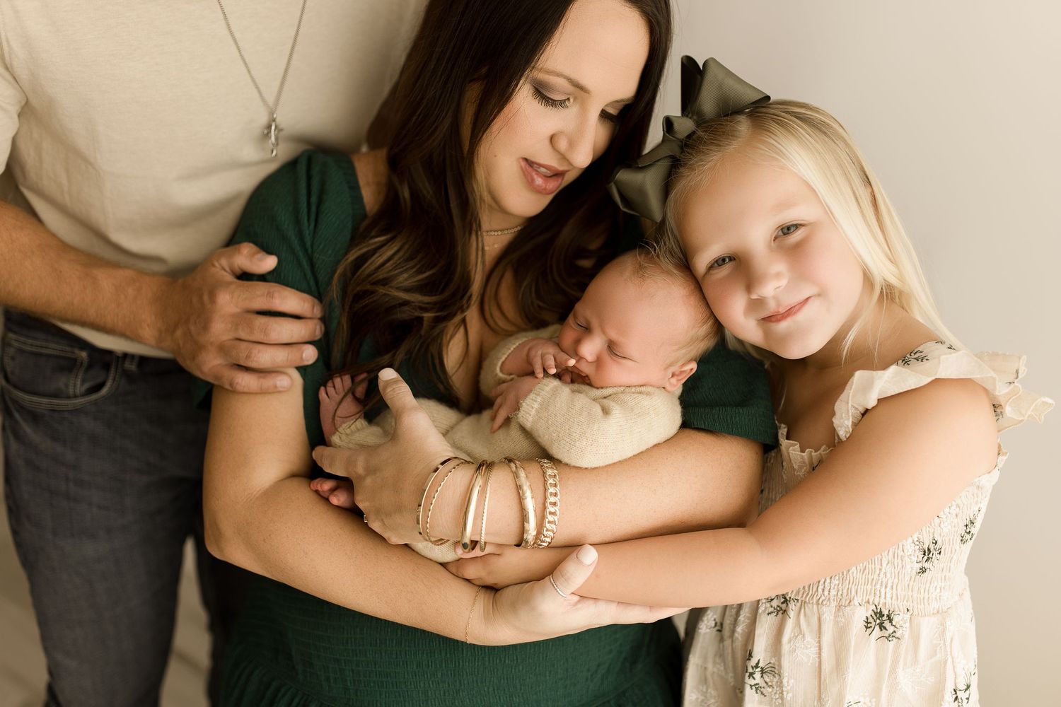 A tender family portrait series showing parents lovingly embracing their newborn baby in intimate indoor settings.