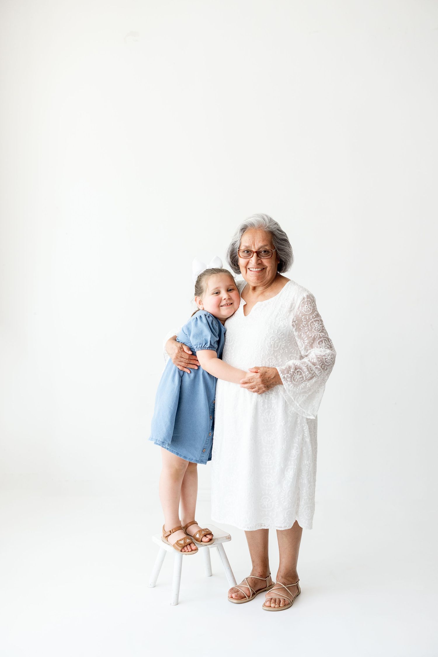 A child wearing blue and an adult in white interact playfully against a bright white studio background.