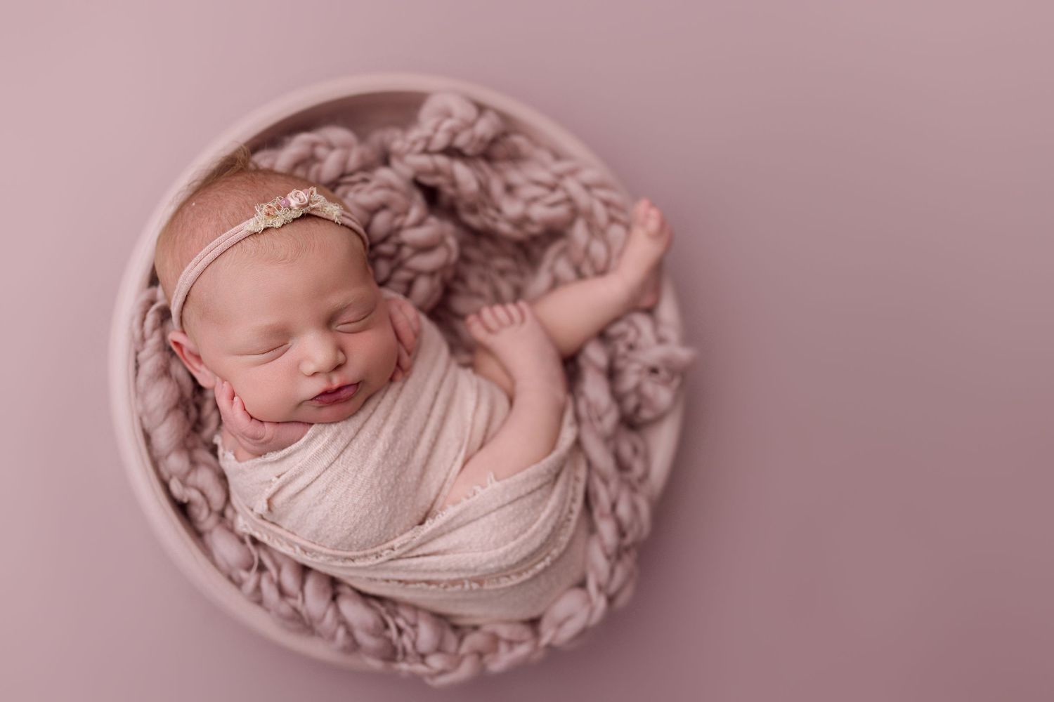 A sleeping newborn wrapped in soft pink fabric against a pink backdrop in a professional studio setting.