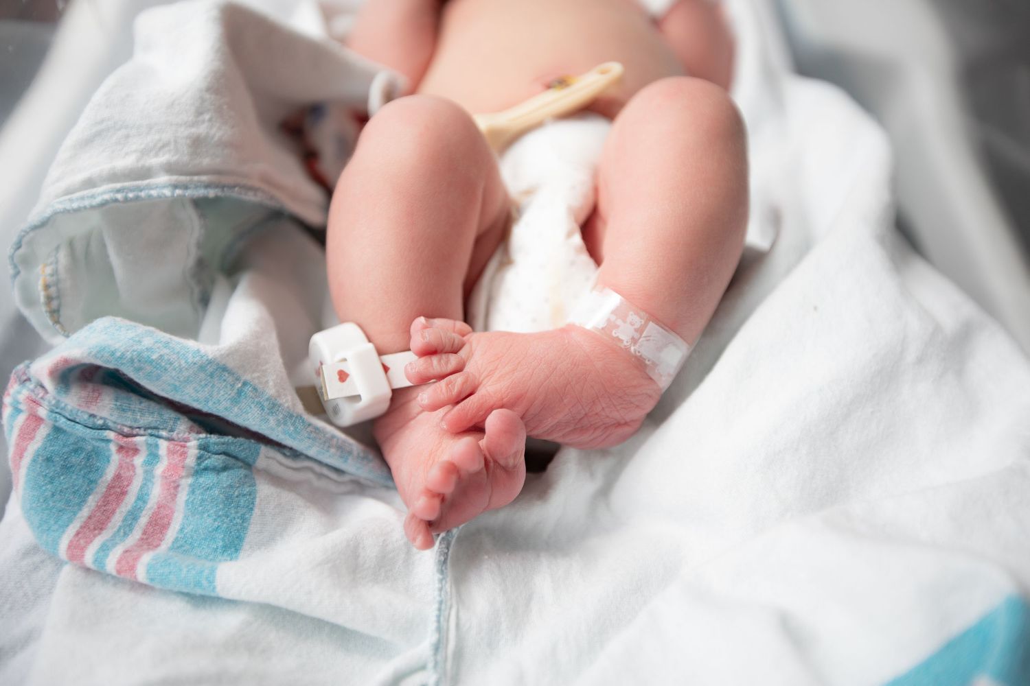 Tiny feet of a newborn baby rest on white hospital linens with blue stripes during Fresh 48 session in Beaumont hospital.