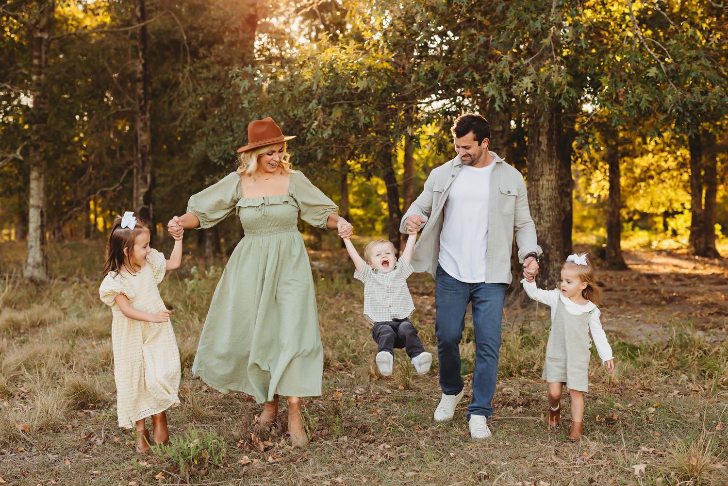 A joyful family walks together holding hands through a sunlit autumn forest path.