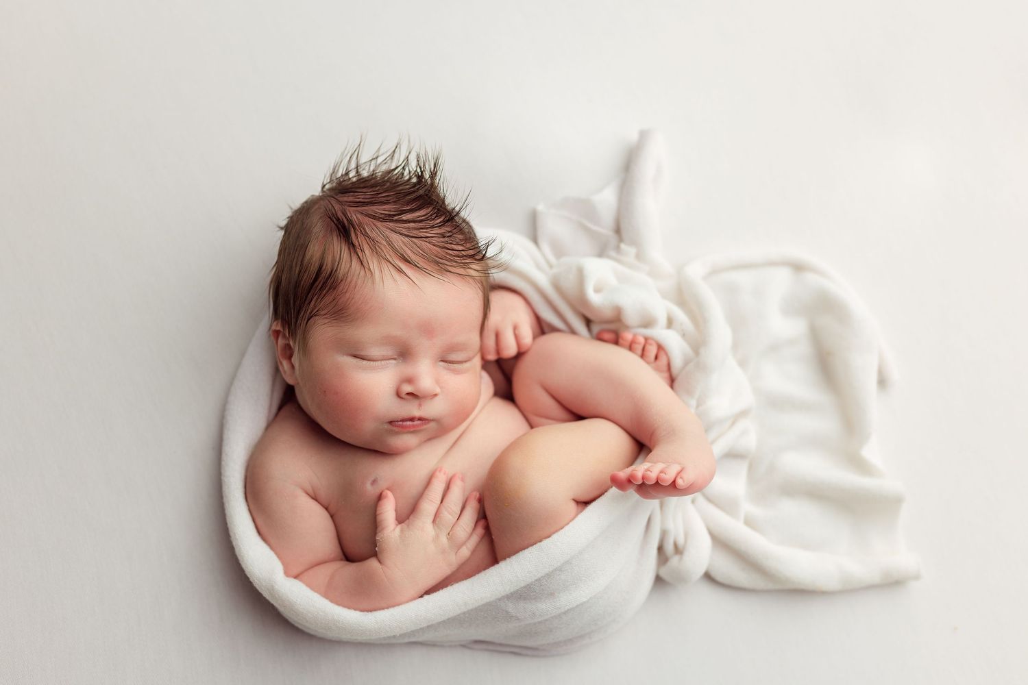 Newborn photography collection showing peaceful sleeping baby wrapped in soft white fabric.