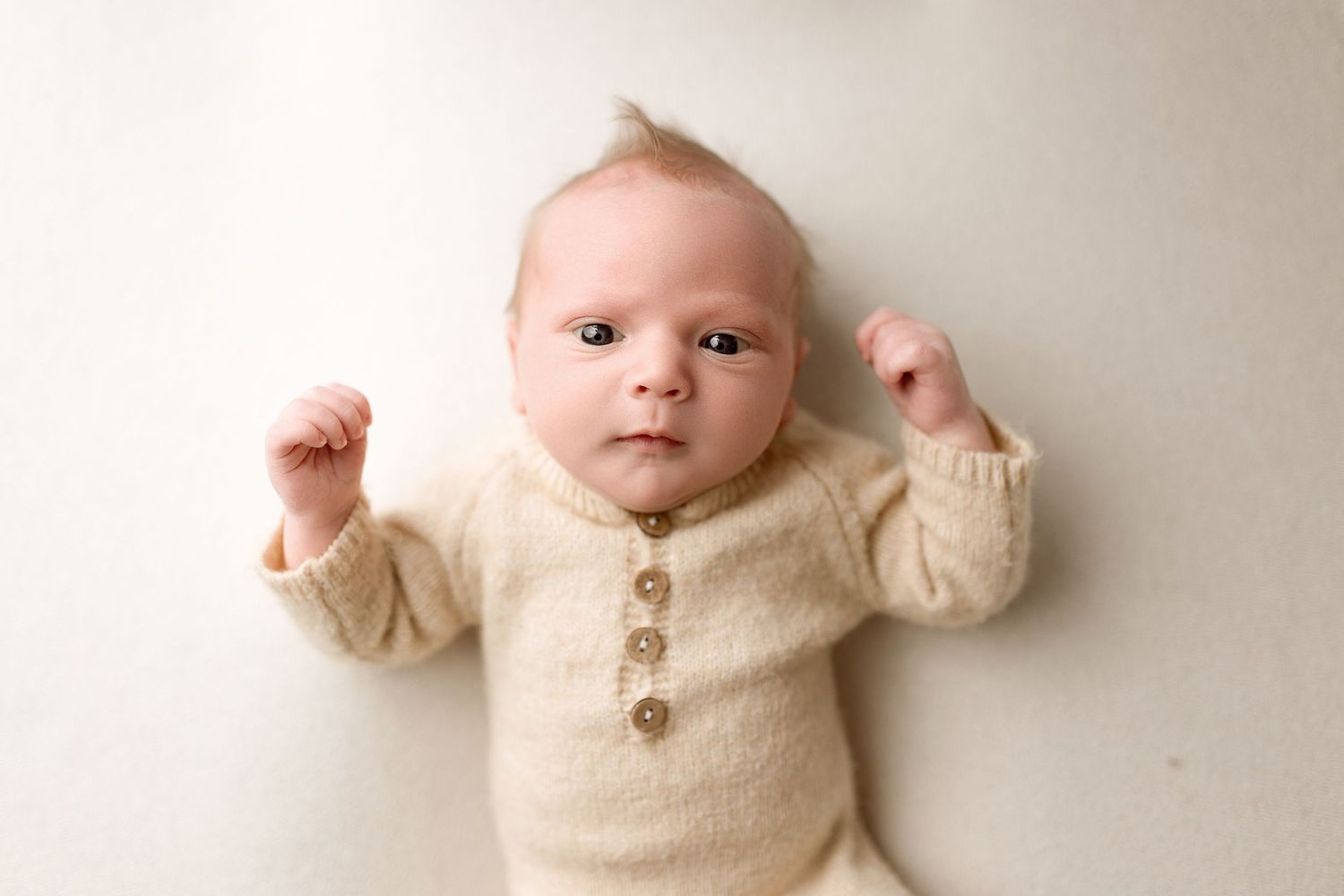 A baby wearing a cozy cream-colored sweater lies on a light beige background in a collage of four similar poses.