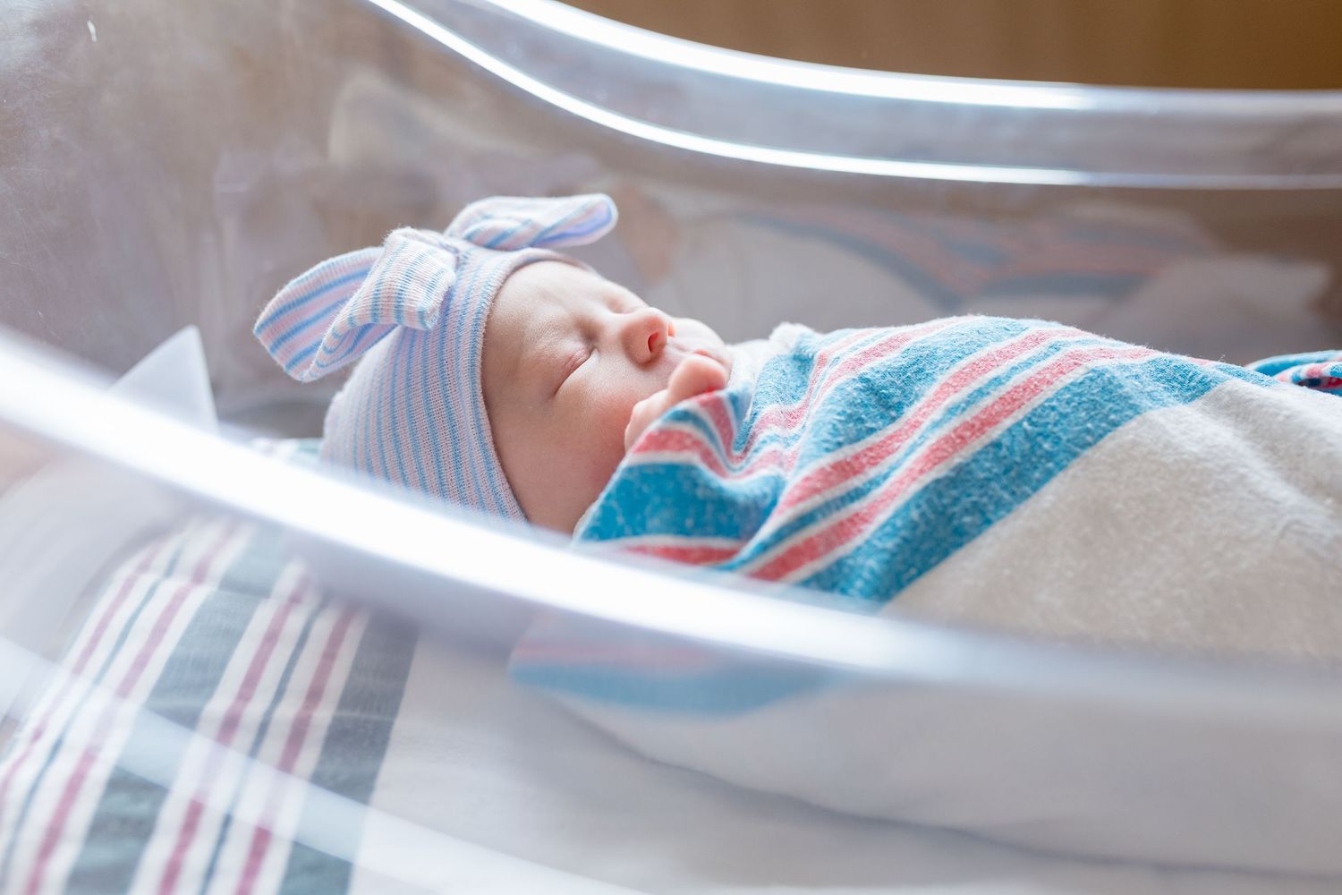 A sleeping newborn swaddled in a blue and pink striped blanket rests peacefully in a hospital bassinet during Fresh 48 session in Beaumont.