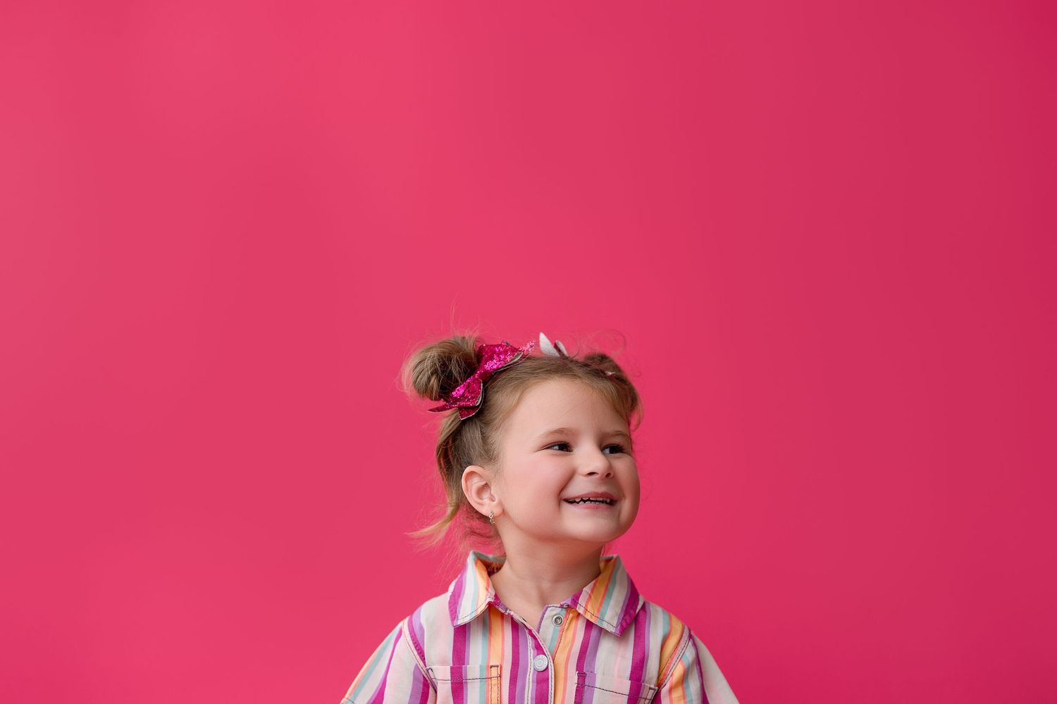 Child spinning with hair flying and arms outstretched on bright pink background.
