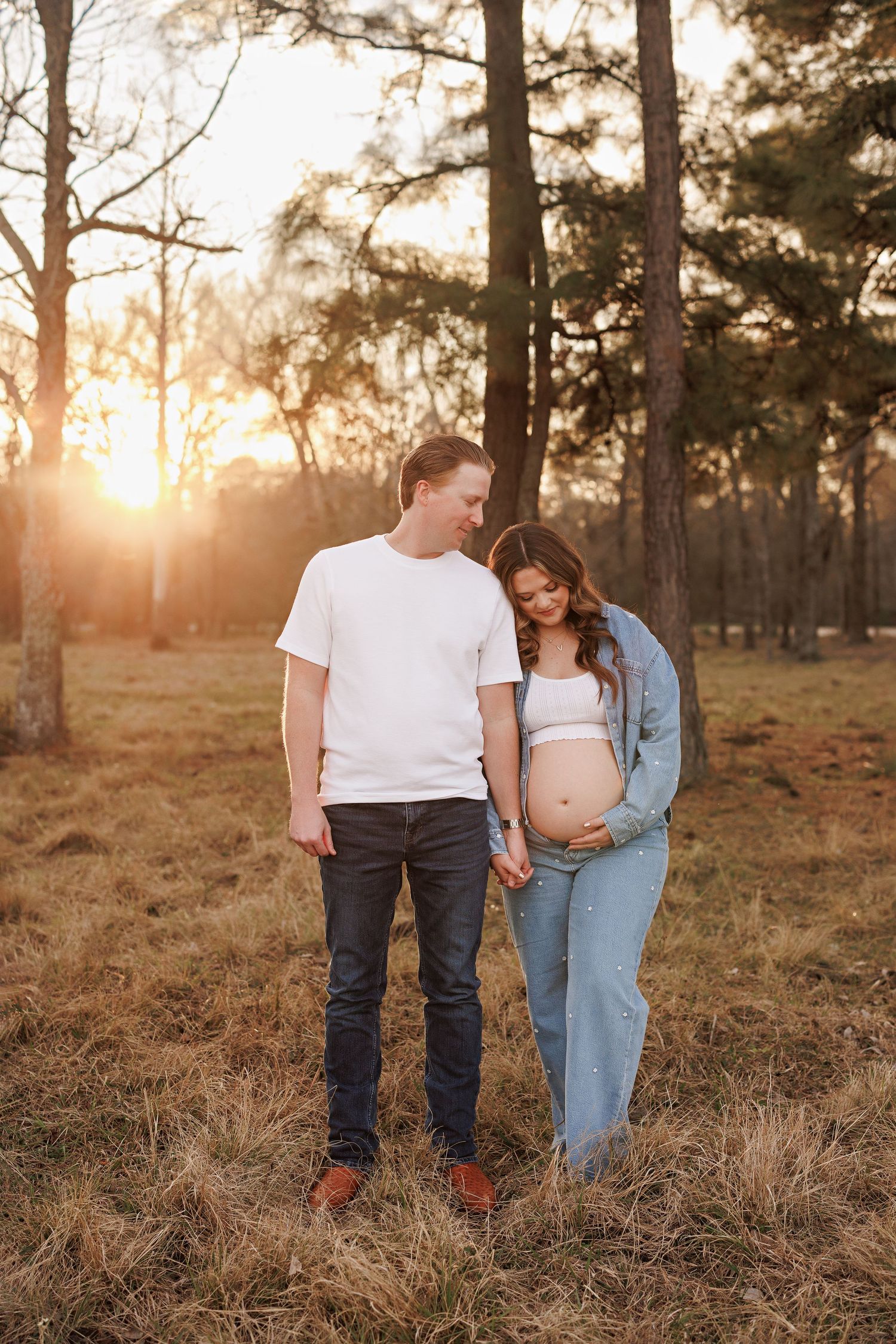 Sunset maternity photo of couple in casual wear among pine trees with Bree Elle Photography in Lumberton, TX.