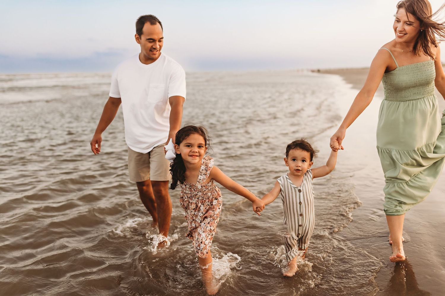 A family splashes and plays together in the shallow ocean waves at sunset.