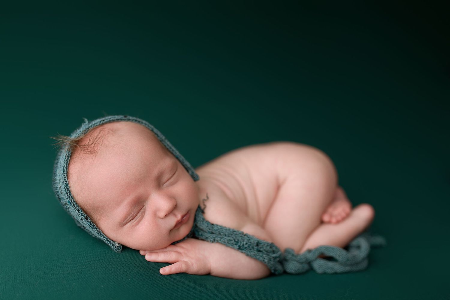 A series of peaceful newborn baby portraits on a dark teal background shows different sleeping positions.
